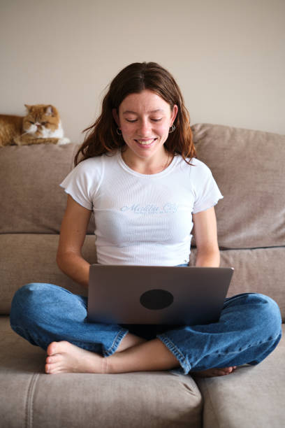 istock Smiling woman using laptop on the sofa with a cat 1631749368