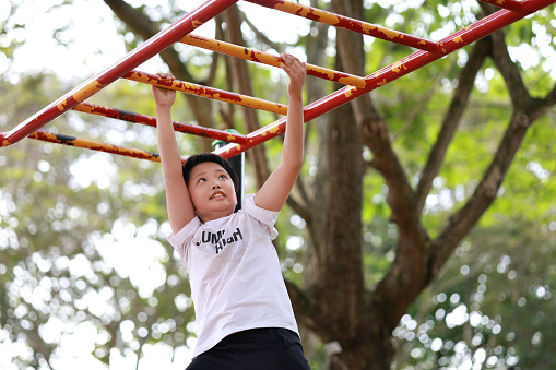 A lively Asian boy confidently navigating the monkey bars at a playground, demonstrating his physical agility and adventurous spirit.