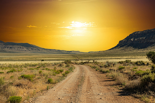 A dirt road stretching across a vast arid valley in northern Arizona into the setting sun with a clear blue sky.