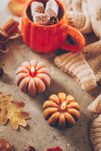 Burning candles shape of pumpking, mug with aiutumn drink, leaves and cinnamon.