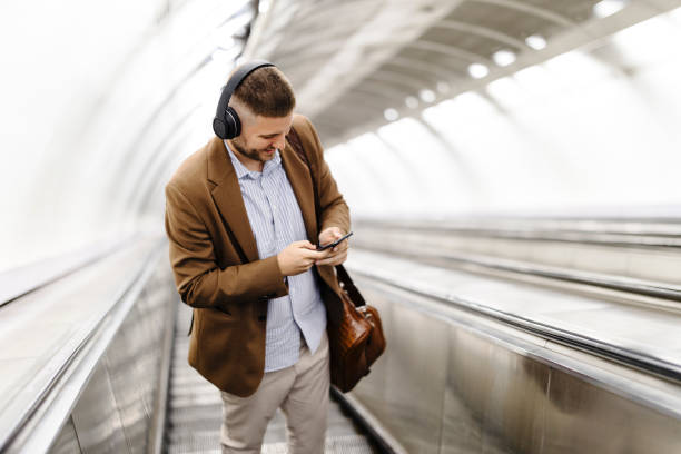 man standing on escalator on his way to modern brightly lit subway station. public transportation and urban life concept. low angle shot. - brightly lit audio imagens e fotografias de stock