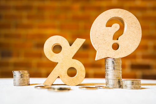 Percentage and question mark with coin on wood table, raising or lowering Fed interest rates to correct inflation concepts.