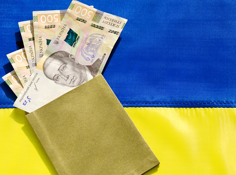 Ukrainian currency hryvnia on the background of the Ukrainian flag. State assistance to citizens in connection with the war in Ukraine.