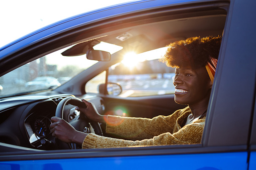 Smiling African-American woman holding the steering wheel and smiling while driving a car, on a nice sunny day