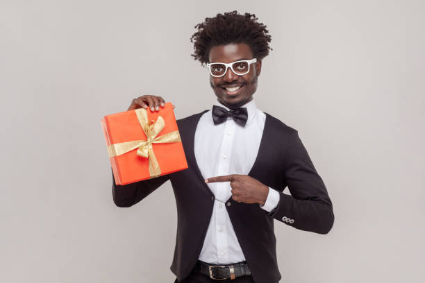 istock Delighted handsome man in glasses standing pointing at gift box congratulating with festive event. 1631861069
