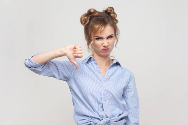 istock Woman shows disapproval sign, keeps thumb down, expresses dislike, frowning face in discontent. 1631861103