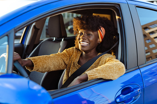 Smiling African-American woman holding the steering wheel and smiling while driving a car, on a nice sunny day