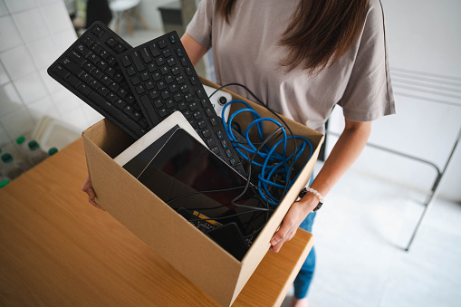 Closed up shot of a woman collecting and holding a paper box with e-waste at home.