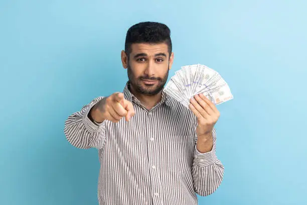 Photo of Businessman pointing to camera and holding dollar banknotes, encouraging to win lottery.