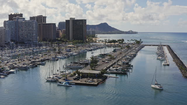 Aerial view of boats and yachts moored at a harbor at Waikiki on a clear, blue sky day with high-rise hotels and resorts in background