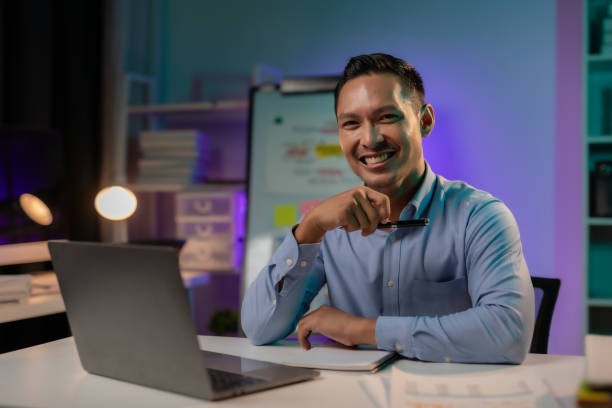 istock Commitment Asian businessman sitting at desk in office Working overtime late at night with document and laptop computer. Overtime work concept. 1631894067