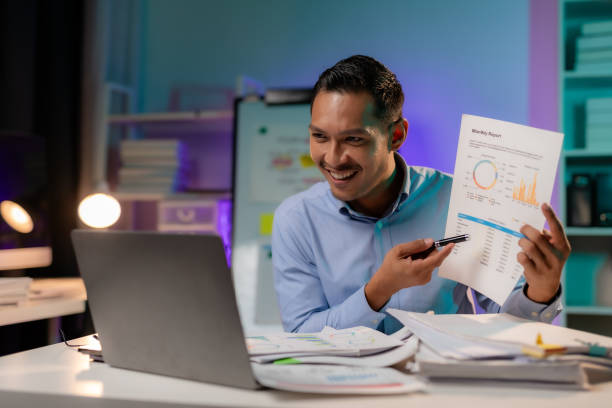istock Serious young Asian male worker working alone with computer and documents in office at night. Focused worker busy managing deadlines staying late at work. Workaholic concept. 1631894628