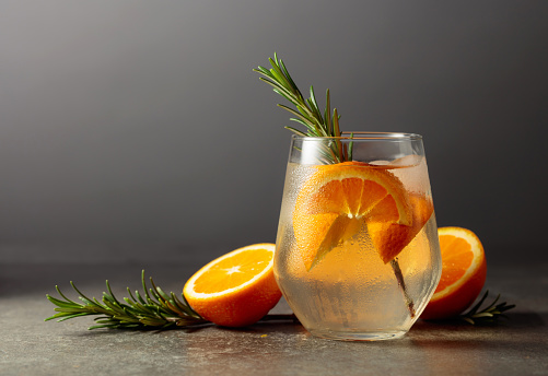 Cocktail gin tonic with ice, rosemary, and orange on a stone table. Copy space.
