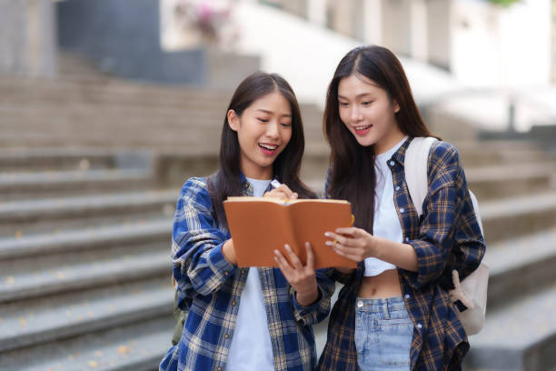 istock Two Asian students stand reading a book together in university. Young Asian Learners Reading Together at University 1631898788