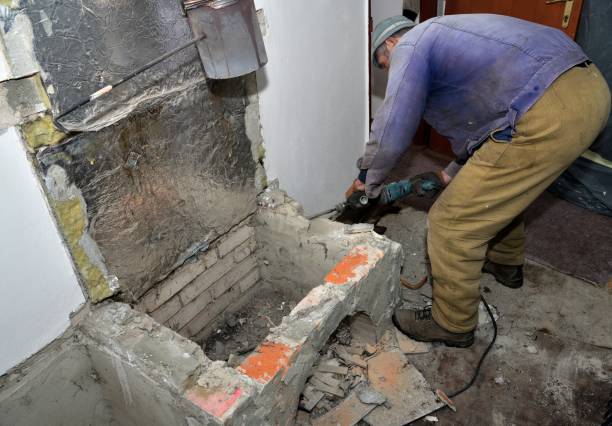 A bricklayer uses a jackhammer to break a wall in a house while building a fireplace stock photo