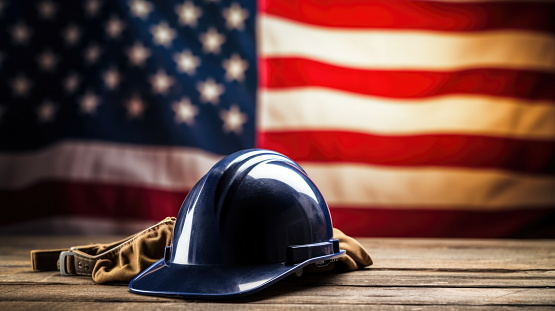 A 3D render of a worker's/engineer's helmet on a wooden table, with the American flag in the background, celebrating Labor Day