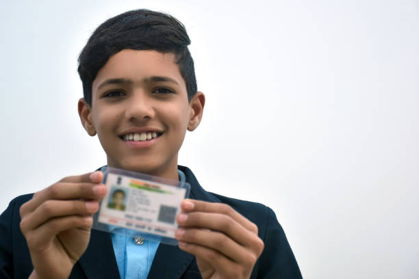 istock Indian school boy wearing dark blue school uniform, with smiling face shows her blurred aadhar card in her hand. sky background 1631949351