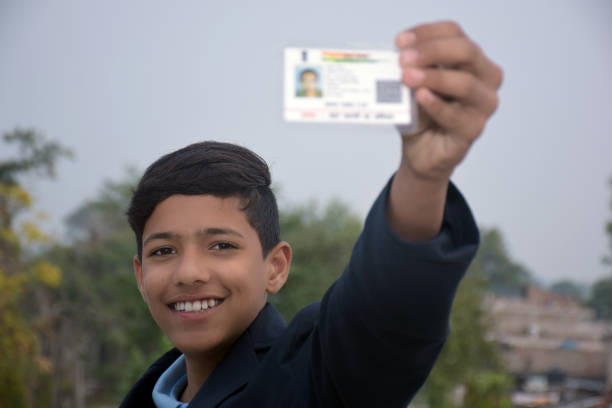 istock Indian school boy wearing dark blue school uniform, with smiling face shows her blurred aadhar card in her hand. blurry background 1631949352