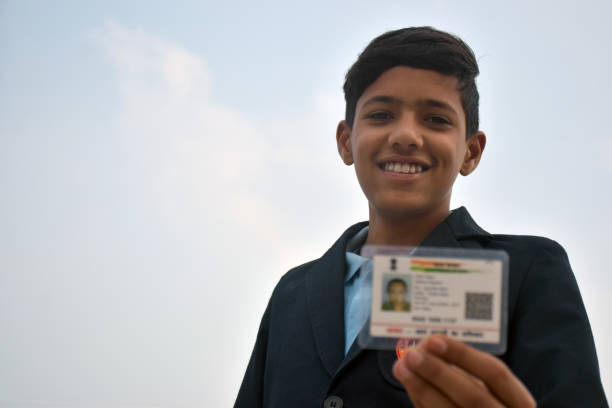 istock Indian school boy wearing dark blue school uniform, with smiling face shows her blurred aadhar card in her hand. sky background 1631950919