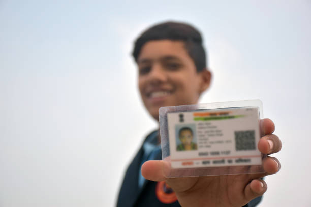 Indian school boy wearing dark blue school uniform, with smiling face shows her blurred aadhar card in her hand. sky background