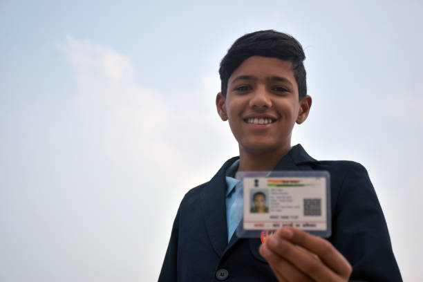 istock Indian school boy wearing dark blue school uniform, with smiling face shows her blurred aadhar card in her hand. sky background 1631950930
