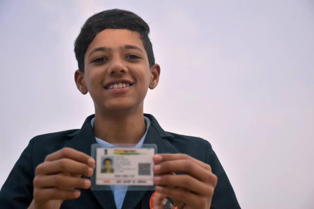 istock Indian school boy wearing dark blue school uniform, with smiling face shows her blurred aadhar card in her hand. sky background 1631950933