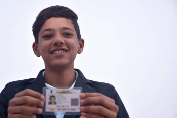 istock Indian school boy wearing dark blue school uniform, with smiling face shows her blurred aadhar card in her hand. sky background 1631951330