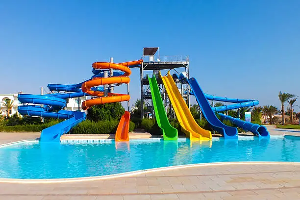 Colorful water slides in water park pool on beautiful summer day. No people, vibrant colors.