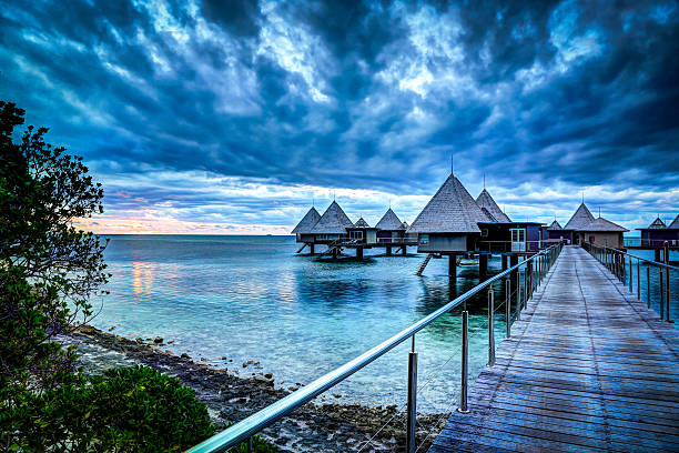 Tropical Paradise Luxury Over Water Resort at Sunset DSLR picture of a Luxury over water bungalow inside a lagoon at sunset.  The bungalow is in the foreground, the water is reflecting the sky. The sky is dark blue and orange.  new caledonia photos stock pictures, royalty-free photos & images