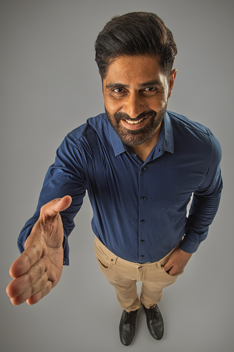 High angle portrait of smiling male manger giving handshake while standing against white background
