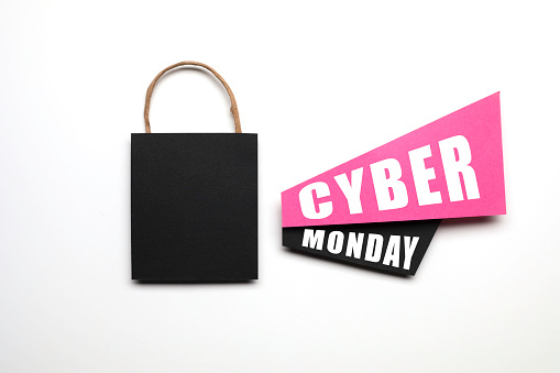 Black shopping bag, pink and black  papers with announcement effect and Cyber Monday text on it on white background.