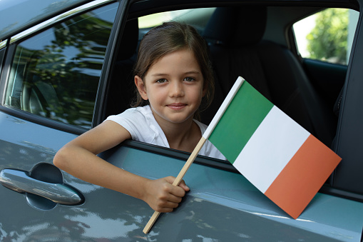 Girl in car is holding Italian flag with a toothy smile.