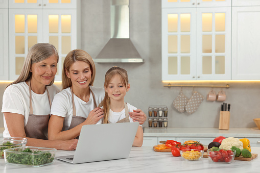 Three generations. Happy grandmother, her daughter and granddaughter using laptop in kitchen