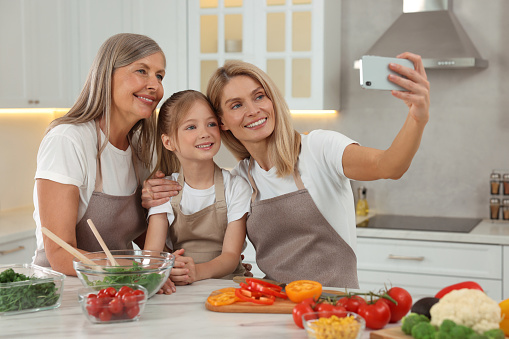 Three generations. Happy grandmother, her daughter and granddaughter taking selfie while cooking together in kitchen
