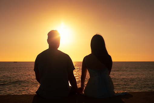 Couple holding hands on the beach and watching beautiful sunset.