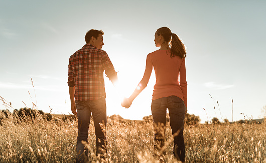 Couple holding hands in the field at sunset.