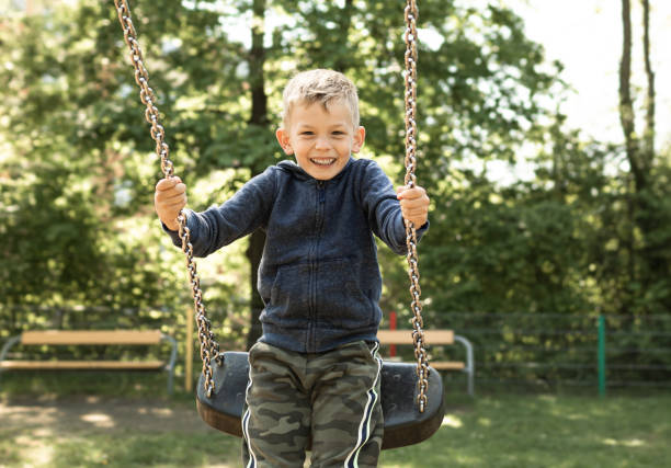niño feliz columpiándose en el columpio en el patio de recreo. - child swing swinging spring fotografías e imágenes de stock