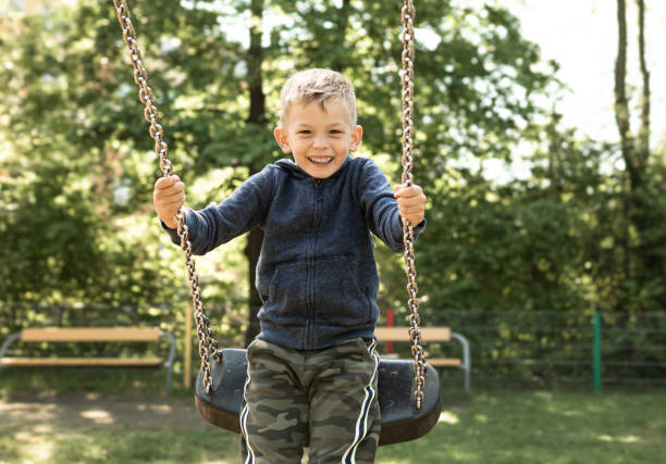 Ragazzo felice che oscilla sull'altalena nel parco giochi. - foto stock