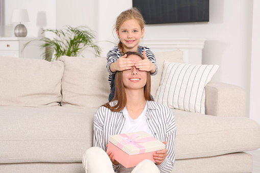 Cute little girl presenting her mother with gift on sofa at home