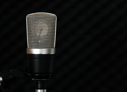 Condenser microphone with a large golden diaphragm on a dark background of the soundproof surface of the studio wall