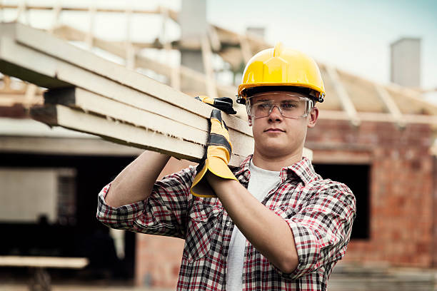 joven trabajador de construcción de transporte de tablas de madera - madera material de construcción fotografías e imágenes de stock