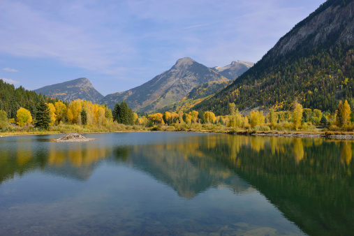 lake with reflection of the mountains and golden, green and red aspen in Colorado during foliage season