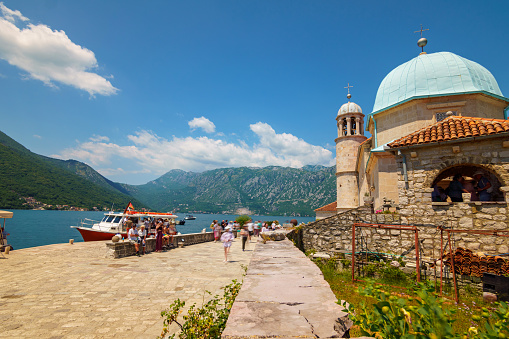 Church of Our Lady of the Rocks on the Island of Saint George, Bay of Kotor near Perast, Montenegro - June 27, 2023: crowds of tourists come by ships near the historic church, a bright sunny day, travel