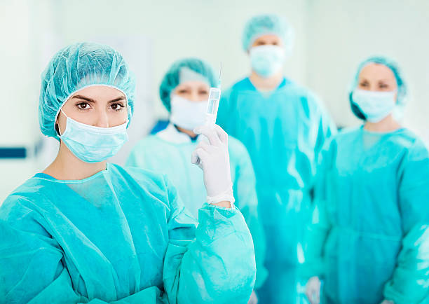 Surgical team in scrubs before starting surgery Young female surgeon holding syringe with medical team in back nurse smock stock pictures, royalty-free photos & images