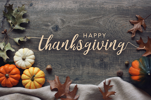 Feliz día de Acción de Gracias texto de caligrafía de tarjeta de felicitación con calabazas de otoño, calabaza, manta cálida y acogedora y hojas sobre fondo de mesa de madera oscura photo