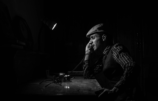 Image of man during the 1940s shouting at the phone. Vintage and retro black & white image of a man dressed as peaky blinders talking in the phone while fixing an old camera