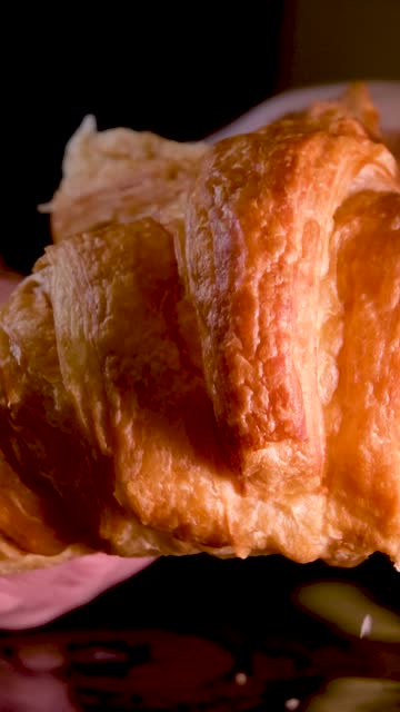 female hands break a fresh warm croissant delicious breakfast homemade cakes on a black background crumbs falling on a stone table are visible light structure porous pastries bread dessert