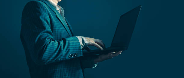 istock Businessman standing sideways holding and typing laptop computer. 1632153235