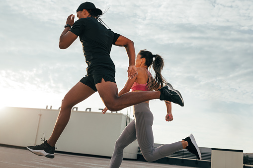 Fitness couple running and jumping on the roof. Athletes sprinting on the roof at sunset.