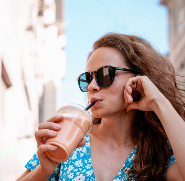 istock Brunette curly woman wearing sunglasses doing smoothie with straw. 1632166916